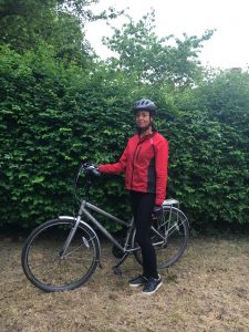 Photograph of woman wearing cycle helmet and red jacket with bike